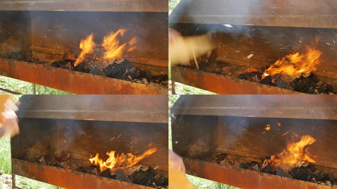 烤肉串人的手在烤肉架上挥舞着一块纸板。烤肉串风扇用平牌在火盆中吹起火焰。慢动作，特写