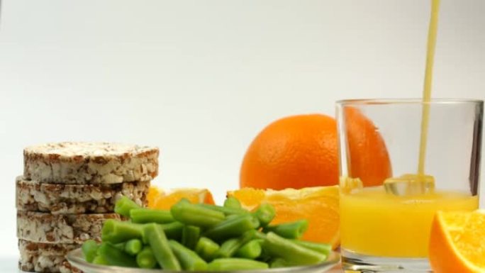将橙汁和健康产品，豆类，面包卷倒入玻璃杯中