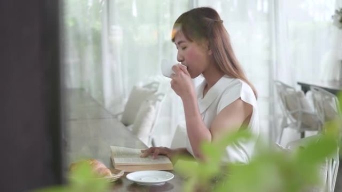 年轻女子在面包店读小说时喝咖啡的侧视图。