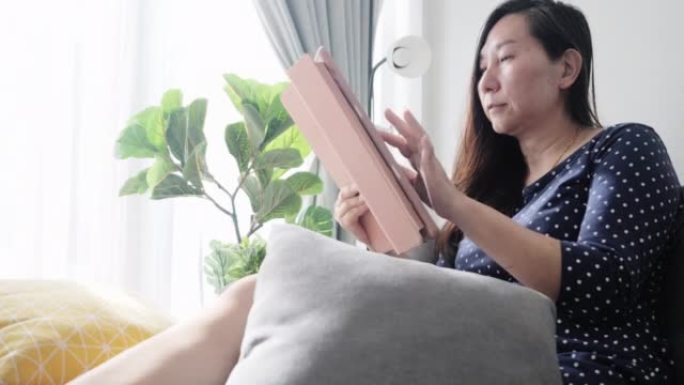 亚洲成年女性坐在沙发上，使用数字平板电脑结算付款或在线购物，生活方式概念。