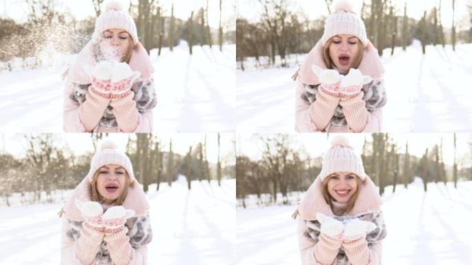 年轻女子穿着柔软的粉红色羽绒服，白帽子，连指手套和围巾在雪地上吹
