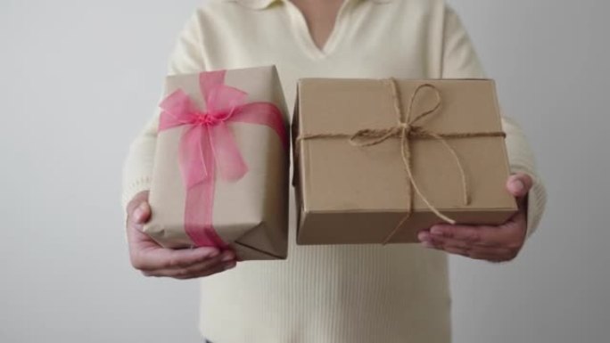 女人拿着和展示两个带粉色丝带的礼品盒