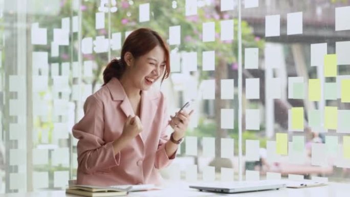 一位亚洲女商人坐在一家公司的私人办公室里，她看着手机上的数据，当她看到公司的利润数据时，她看起来很高
