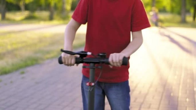 踢踏板车的孩子。夏天，小男孩在公园的小路上骑着踏板车。儿童休闲活动，运动
