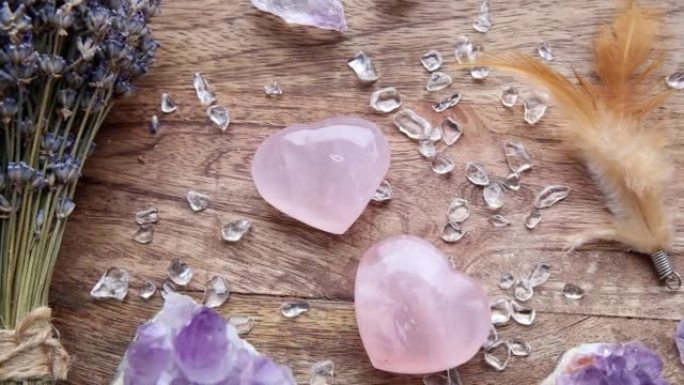 在家里的木托盘上看到两个抛光的粉色玫瑰石英晶体。吸引爱，治愈心轮概念。干薰衣草、羽毛、石屑的花束作为