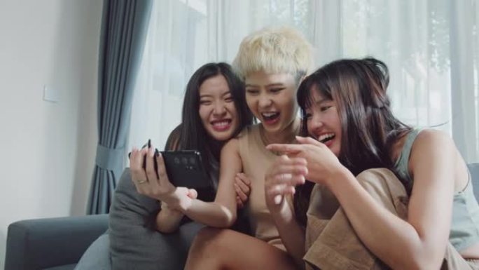 三个微笑的女人朋友坐在家里的客厅里看着智能手机