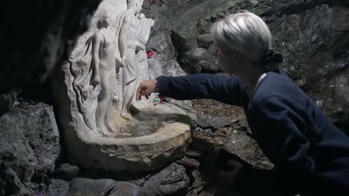 参观罗多彼山脉神秘地下洞穴魔鬼的喉咙洞穴期间的女性传统硬币喷泉，长满落叶和常绿森林Trigradsk