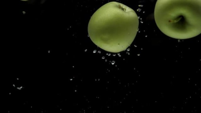慢动作三个青苹果落入黑色背景的透明水中