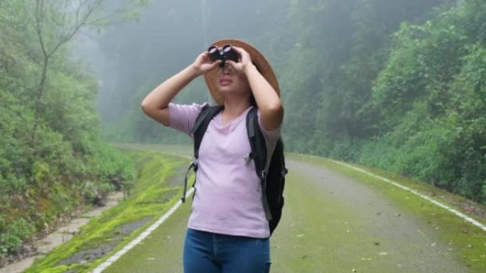 女性环保主义者在雨林中使用双筒望远镜。女探险家使用双筒望远镜旅行，并拥有幸福的微笑。游客透过双筒望远