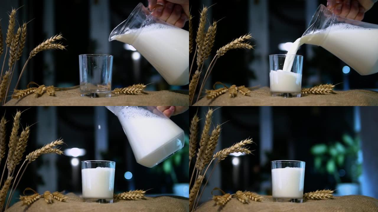 一名男子将牛奶从水罐倒入乡村背景的玻璃杯中，天然乳制品放在稻草桌上的透明玻璃杯中