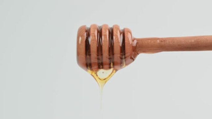 健康食品概念。美味的甜液体蜂蜜从白色背景上的木勺流下来。有机健康蜂蜜，维生素，甜食。从勺子里滴下来的