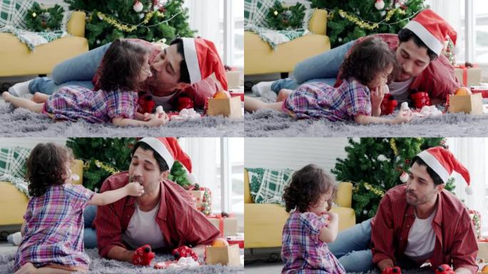 父亲在公寓客厅的欢乐圣诞节庆祝活动中照顾蹒跚学步的女儿。新年派对上家庭幸福。小女孩喜欢和爸爸一起玩。