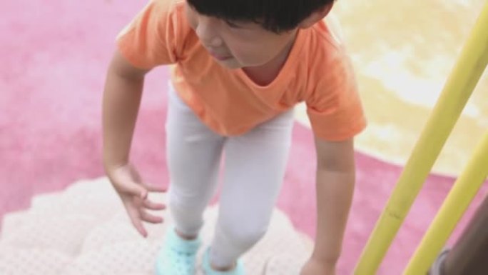 4k视频慢动作亚洲儿童穿着橙色t恤在操场上玩耍。