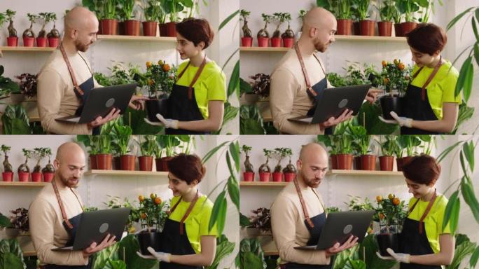 e花卉商店的老板用笔记本电脑在他的商店里做库存，花店女士帮助他拿着花盆