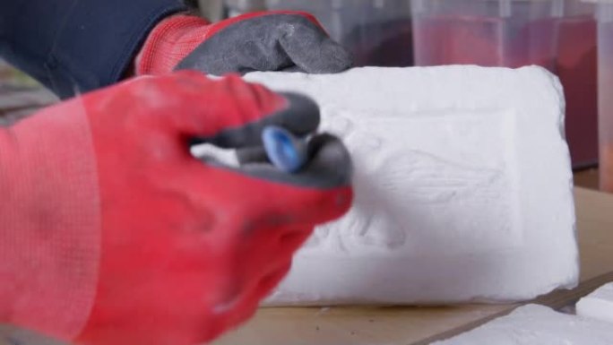 戴着手套的工人用一只手拿着基于带有双头鹰标志的砖块的瓷砖，并用其他方法用刷子，特写，慢动作清洁表面残