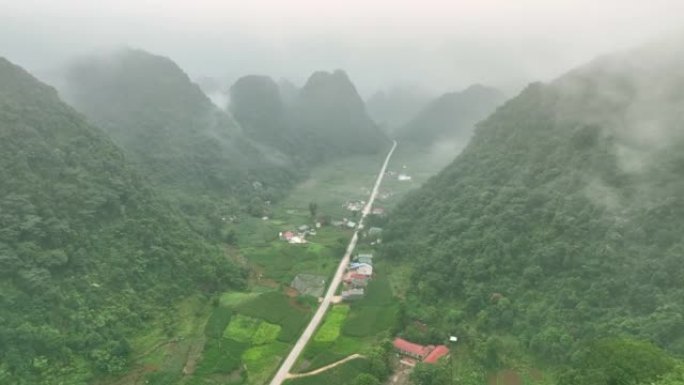 无人机在雾蒙蒙的雨林树木附近的雾蒙蒙的蜿蜒山路上飞行。电影镜头鸟瞰图雄伟的热带山脉景观。在越南北部