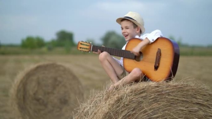 小男孩抱着吉他在干草堆上。