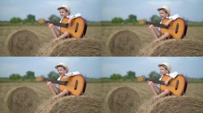 小男孩抱着吉他在干草堆上。