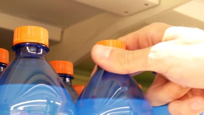 商店货架上蓝橙色塑料瓶汽水的特写镜头，一名男性买家拿走了一个