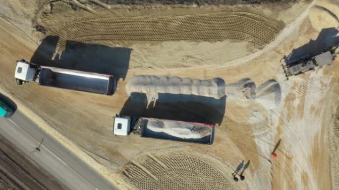 自卸车的鸟瞰图正在从建筑工地的拖车上卸下砾石，以进行新的交通回旋处