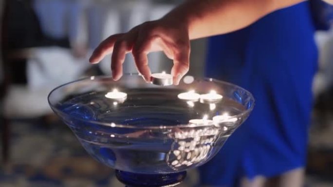特写，男人的手放下燃烧的蜡烛到大玻璃碗里的水