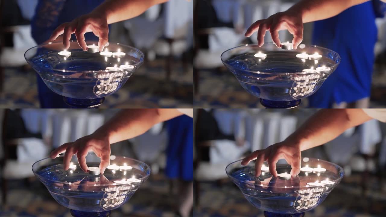 特写，男人的手放下燃烧的蜡烛到大玻璃碗里的水