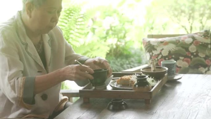 老年妇女在露台上吃油炸猪肉米饭日本食物。成熟的退休生活方式