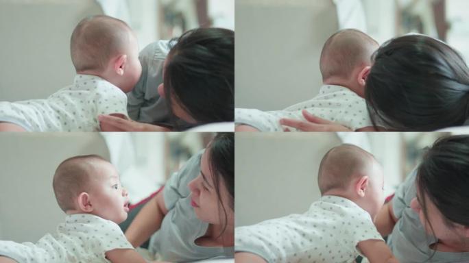 可爱的亚洲新生男婴躺在白色床上和妈妈玩耍，笑容满面。而你妈妈在附近照顾。小无辜的新生婴儿可爱的孩子。