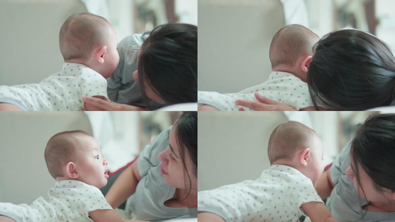 可爱的亚洲新生男婴躺在白色床上和妈妈玩耍，笑容满面。而你妈妈在附近照顾。小无辜的新生婴儿可爱的孩子。