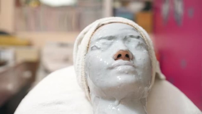 年轻的亚洲妇女在水疗中心使用带有头部按摩的凝胶面膜