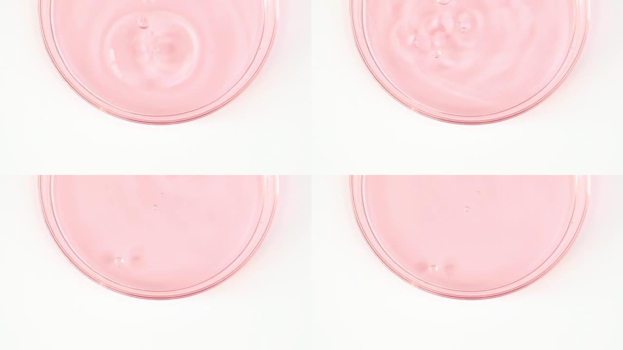 透明的粉红色化妆品液体滴在玻璃碗中的Petri。宏丸血清、乳膏、透明质酸。有机化妆品，药品。慢动作