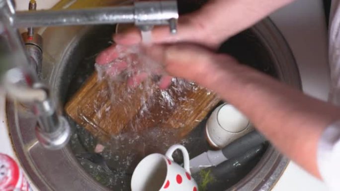 脏盘子被倒入水。一束水从水龙头倒入厨房水槽的脏盘子上