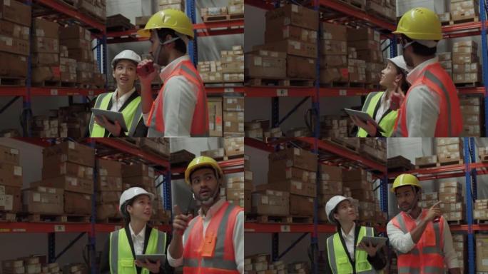 亚洲仓库工人男女在仓库与白色安全帽讨论使用数字平板电脑。仓库员工在分销仓库检查库存。