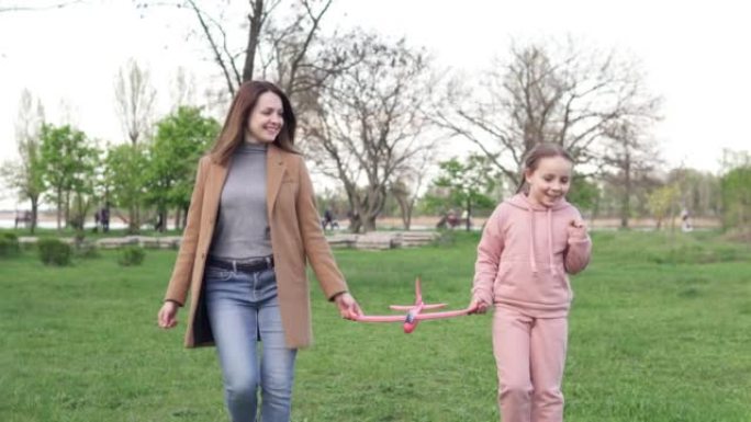 快乐的妈妈和十几岁的女儿在户外玩耍，无忧无虑的家人玩着红色的飞机玩具模型笑着。