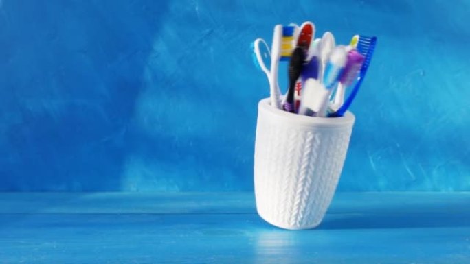 白色杯子中的许多不同牙刷在蓝色背景下在桌子上旋转。4k创意原始视频，具有速度斜坡效果。在高速电影摄像