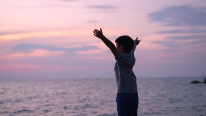 亚洲男孩举起手臂，在海滩上旋转。放松和幸福的概念