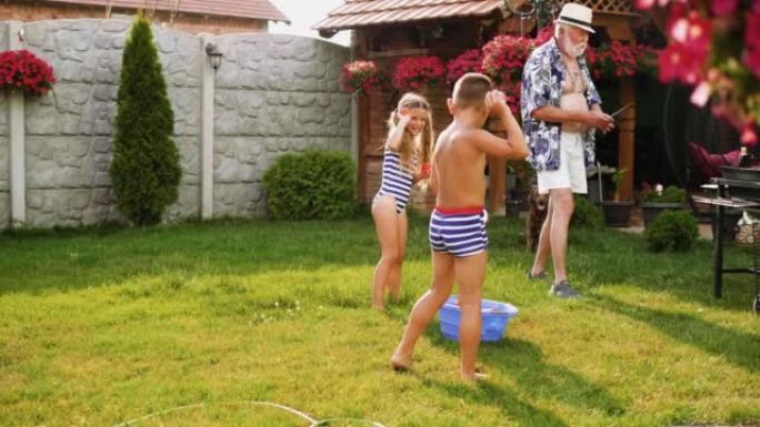 老人正在烧烤，而他的孙子孙女在后院用水气球互相射击