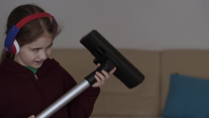 儿童在家庭房间唱歌时使用吸尘器作为麦克风。享受清洁俏皮创意儿童舞蹈。耳机里的小有趣创意女孩用扫帚手柄