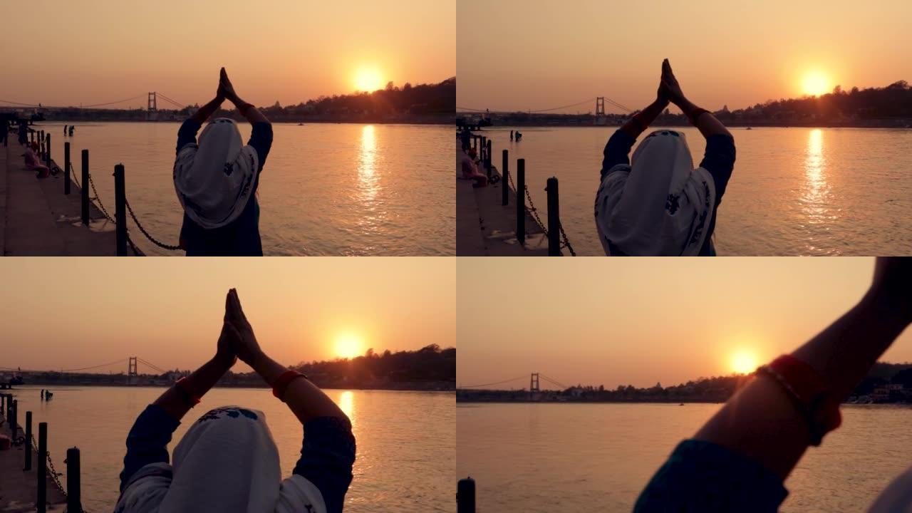 年轻的印度女孩在河岸的地平线上祈祷神圣的恒河和日落