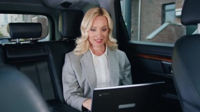 成功的商业女性在现代汽车上笔记本电脑工作。穿着正式西装的白人金发女士坐在后座，在笔记本电脑中搜索信息