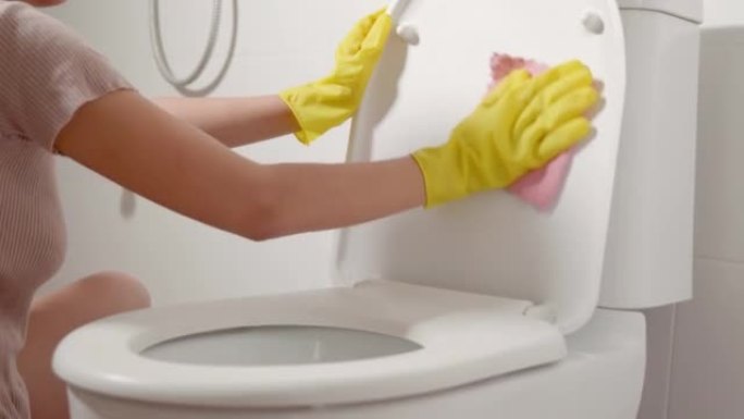 亚洲妇女的手用粉红色的布清洁马桶座圈在家里擦拭洗手间