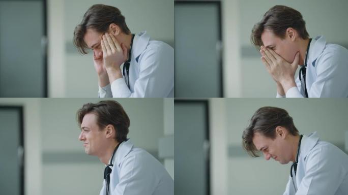 情绪低落的医生坐在医院的诊所走廊上，经历着艰难的情绪。过度劳累的男医生绝望或疲倦地坐着。