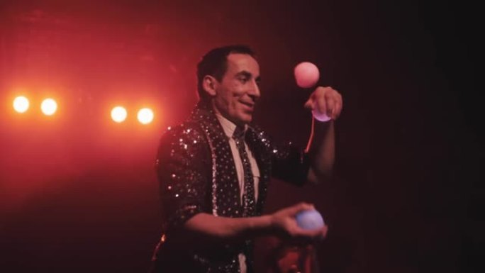马戏团里的一个快乐的人专业地在美丽的灯光下慢动作中杂耍着三个发光球。杂耍演员
