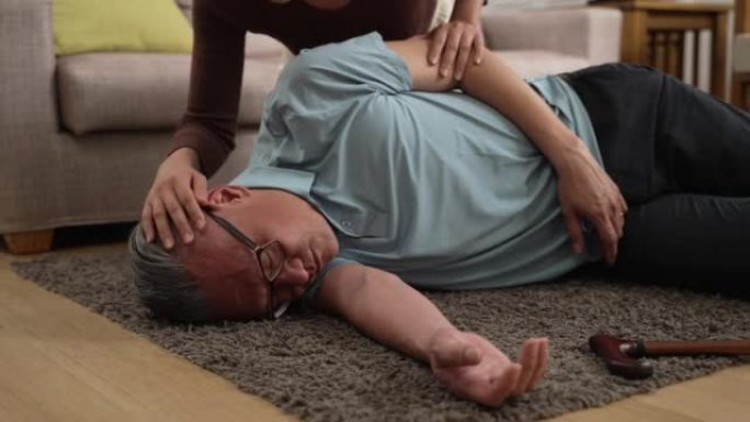 慢动作，特写镜头显示亚洲老人在家中陷入昏迷状态。他家人的手在摇晃他的身体，轻轻地拍打他的脸颊，试图唤