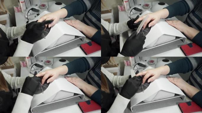 特写视图。美甲师在美容院使用指甲锉。一名白人妇女在美容院修指甲。指甲护理和修指甲