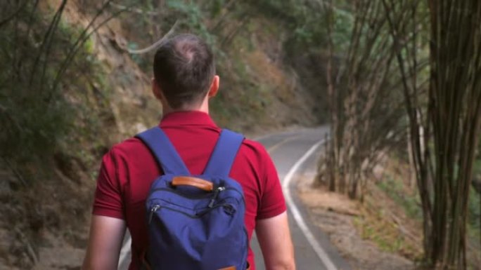 背包客在绿树丛中行走的背包客的背景图。男性旅行者的镜头随后来到国家公园的路上。慢动作