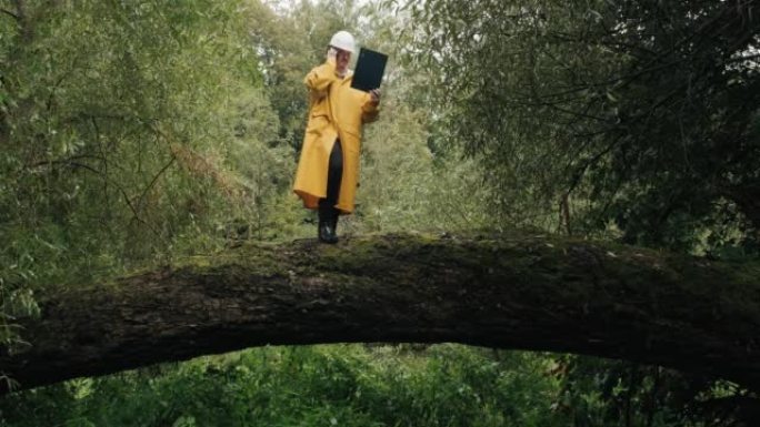 戴着头盔的生态学家站在倒下的树上，他在电话中交谈