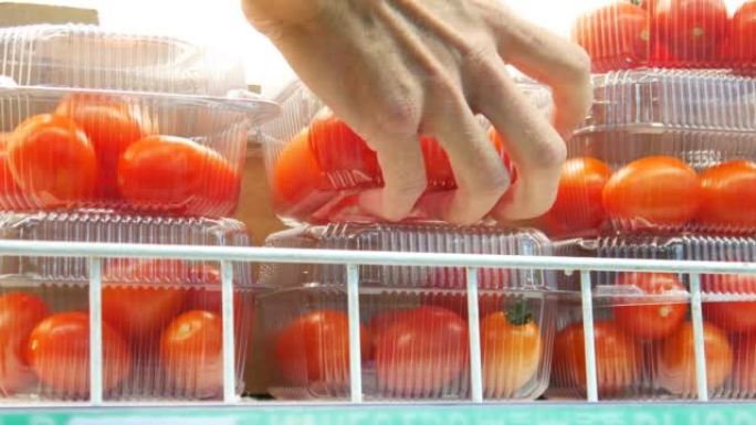 在冰箱架子上的塑料包装盒中的许多小西红柿的特写镜头，一只雄性手拿了一个