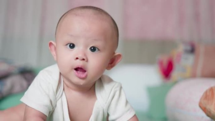 真实的脸部肖像可爱的亚洲新生婴儿在床上爬行或玩耍看着相机，笑容满面。天真的小新婴儿可爱。父母身份和母