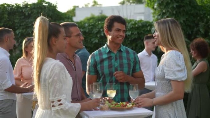 一群多种族的人在夏季享受花园聚会，边聊天边喝酒边吃零食